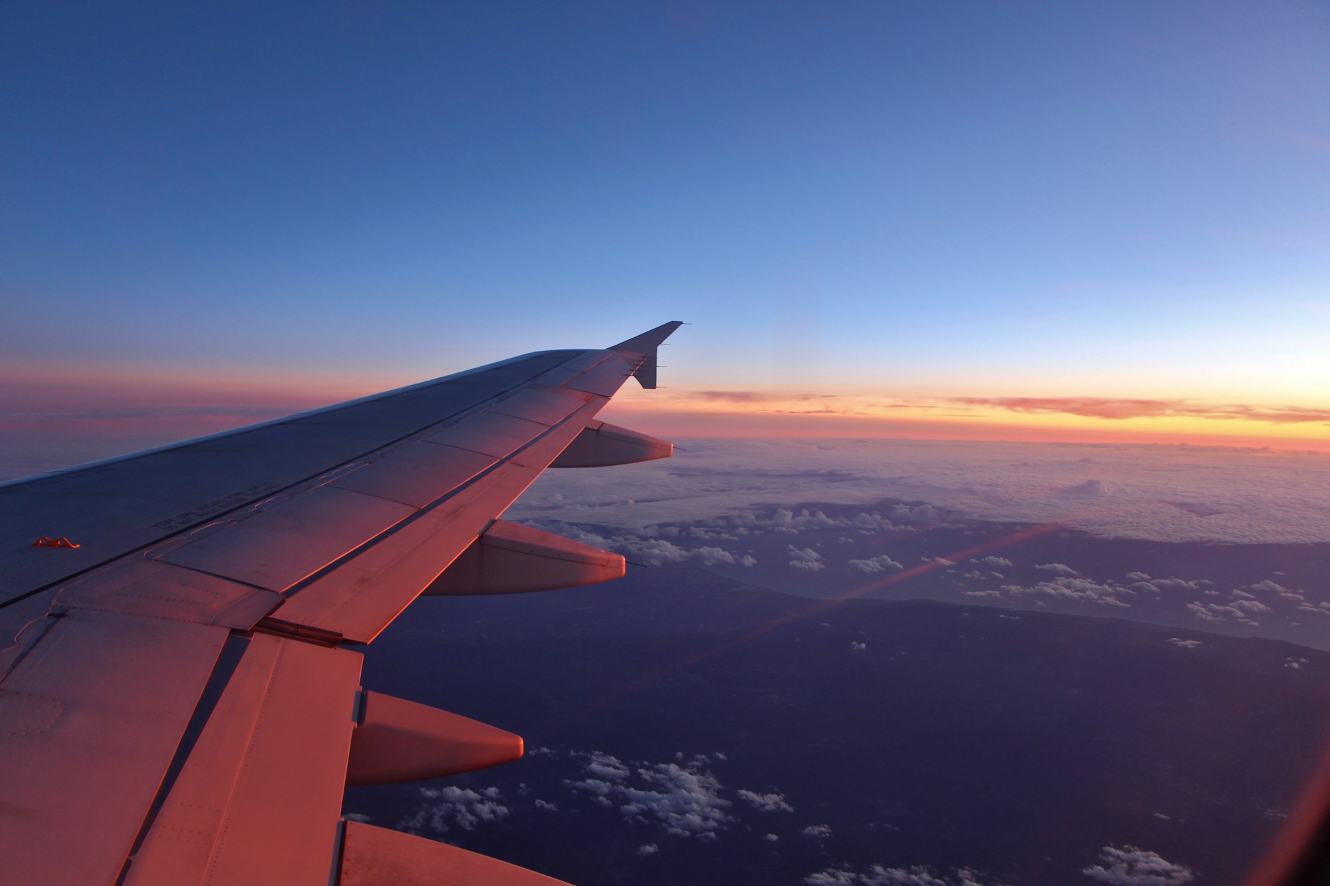 View of an airplane wing at sunset above the clouds